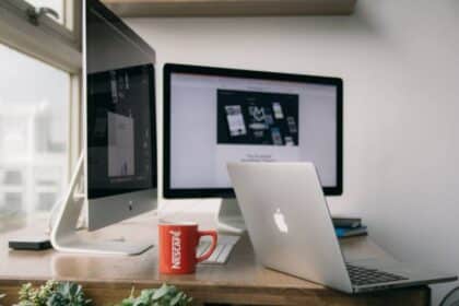 Espace de travail équipé de produits Apple, incluant deux écrans d'ordinateur et un MacBook, sur un bureau en bois.